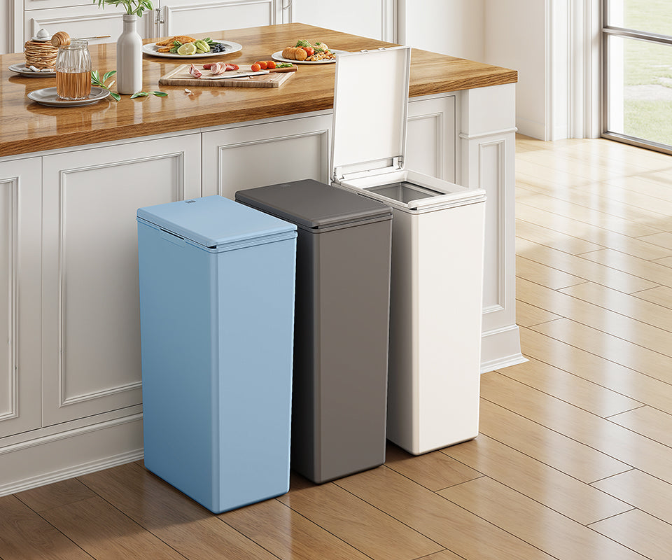 Three slim trash cans in light blue, gray and white beside a kitchen island, one with its lid open