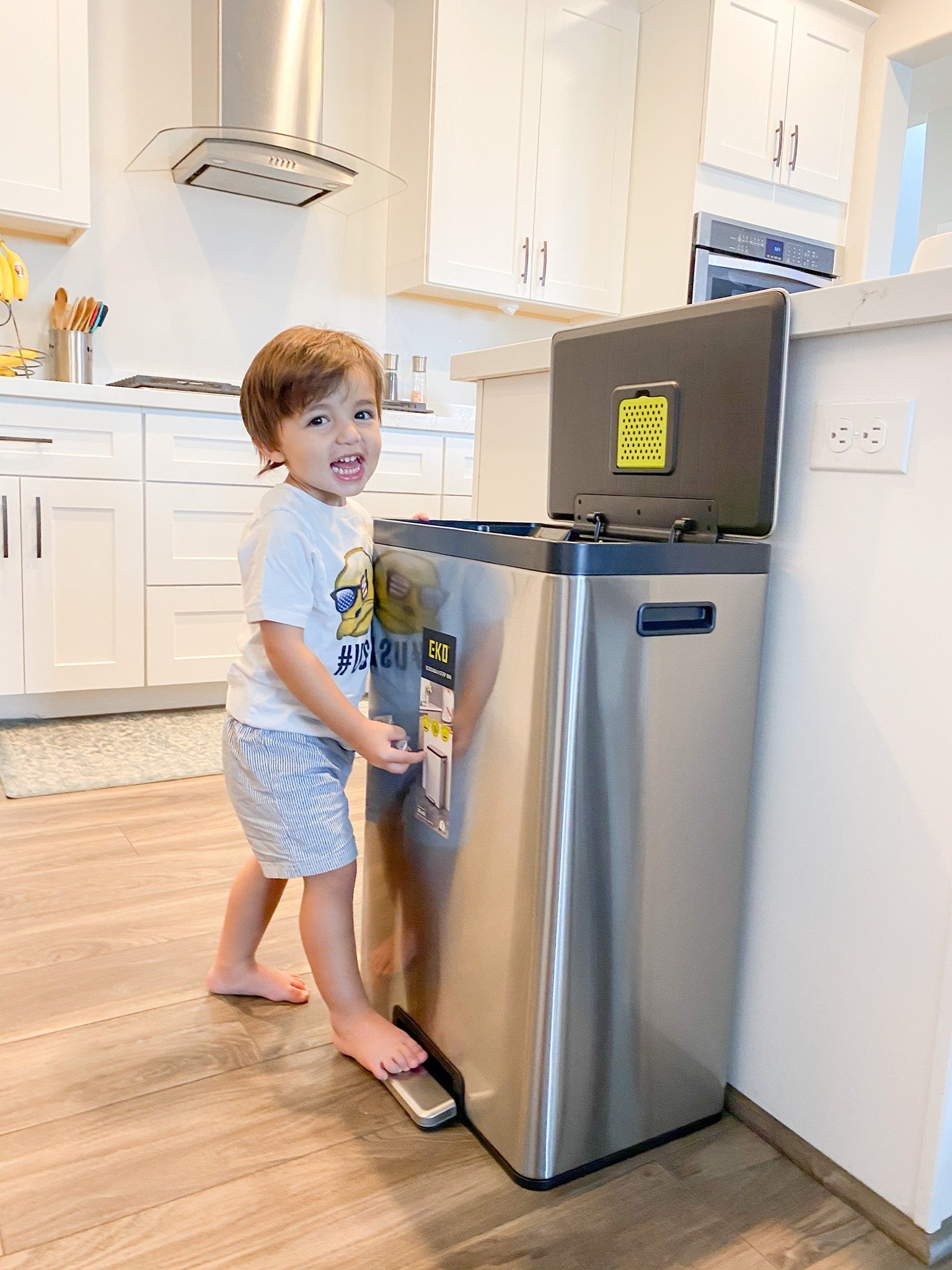 Child interacting with a stainless steel trash can in a kitchen